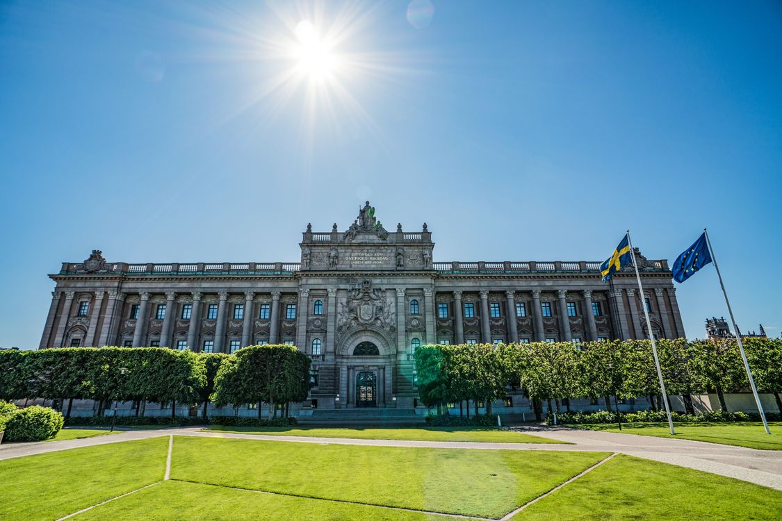 Riksdagshuset i Stockholm med svenska flaggor framför byggnaden.