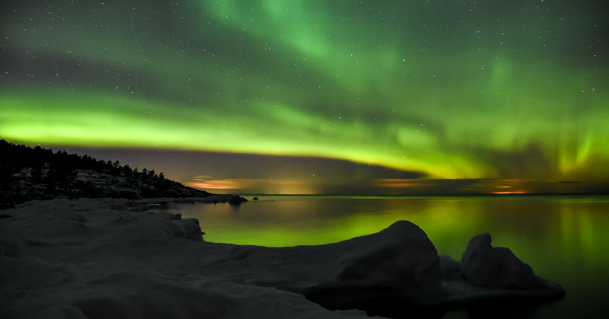 Grönt norrsken över en stilla sjö i Bjuröklubb i Västerbotten under en mörk vinternatt